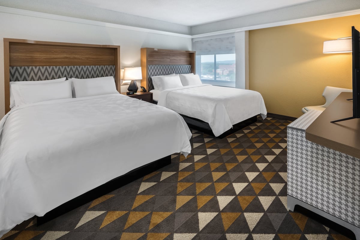 A hotel room with two beds, a desk, a chair, a TV, and a window with a city view.