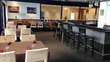 A restaurant with tables and chairs, a bar area, and a view of the street outside.