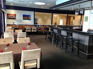 A restaurant with tables and chairs, a bar area, and a view of the street outside. - Holiday Inn & Suites Pittsfield-Berkshires by IHG (Pittsfield)