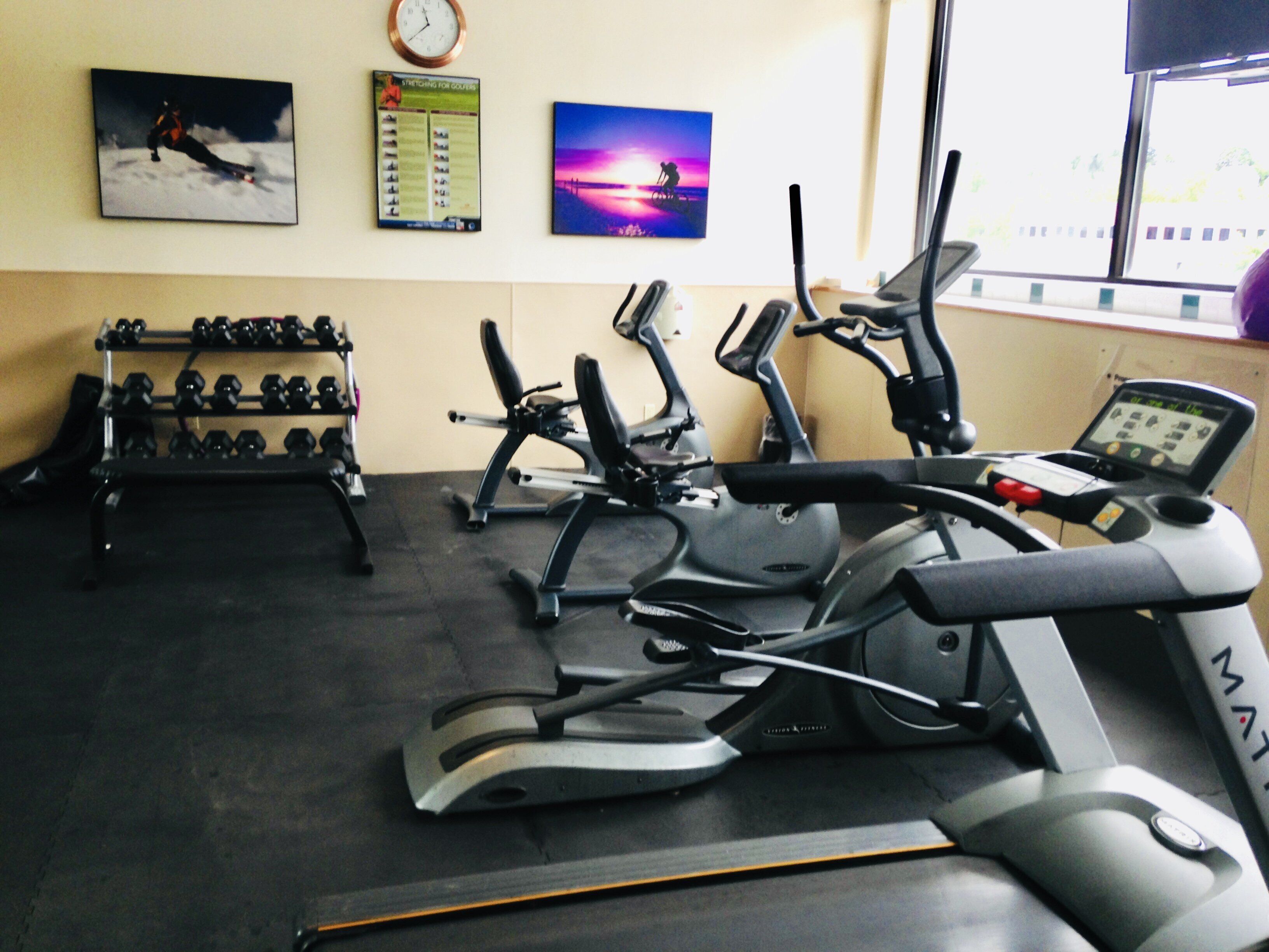 A gym with exercise equipment, a clock, and motivational posters on the wall.