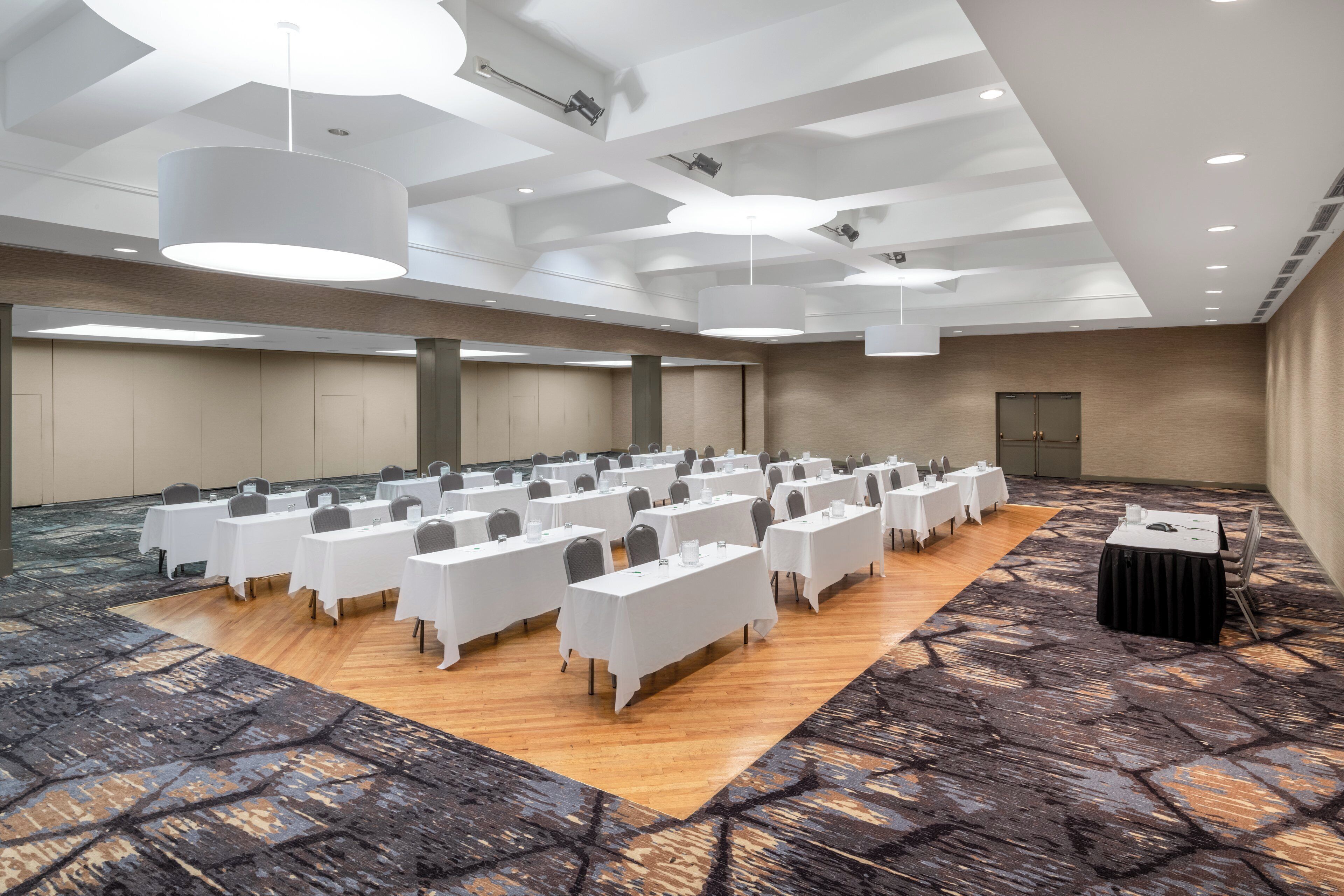 A conference room with rows of tables, a stage, and a carpeted floor.
