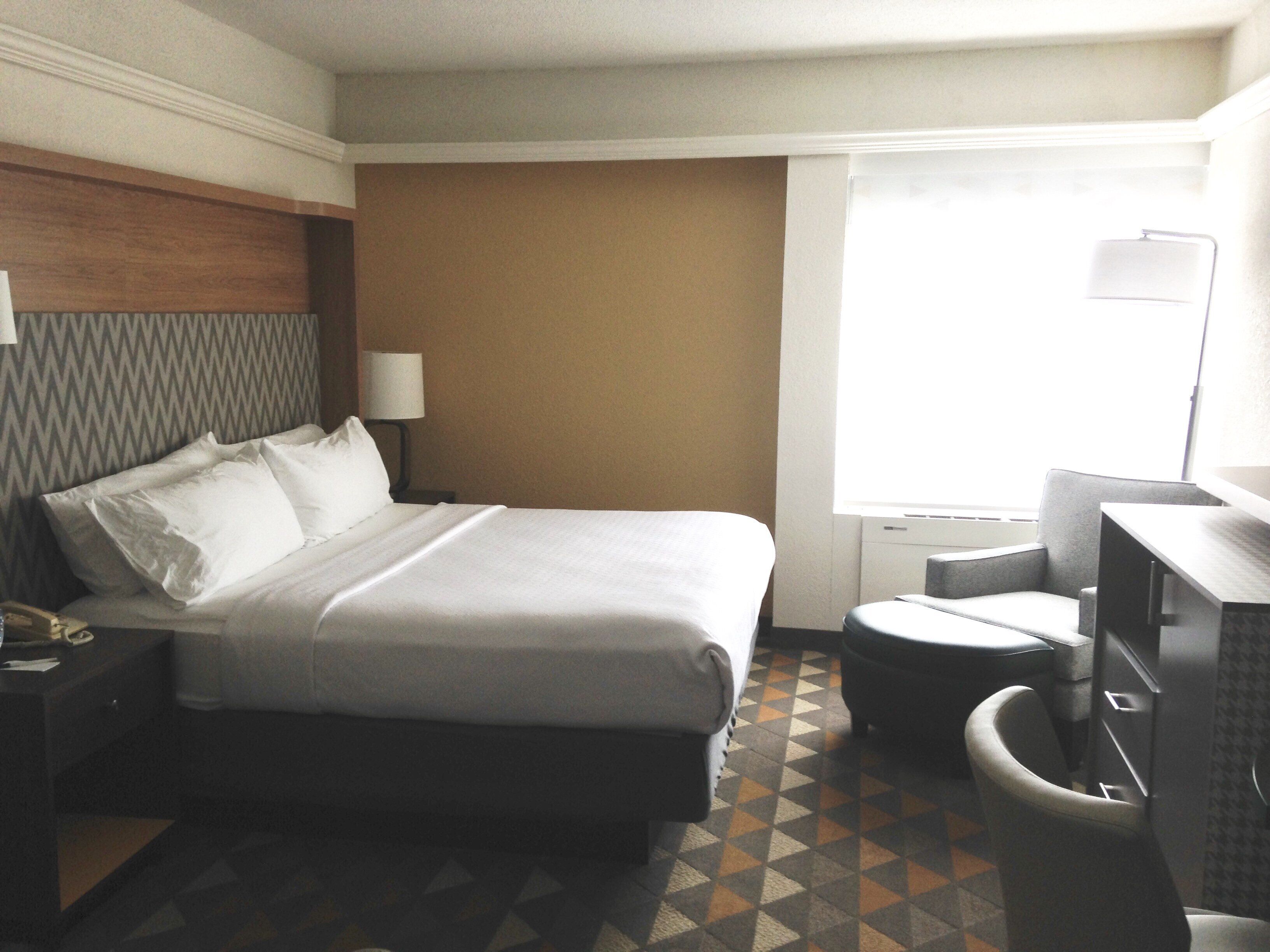 Habitación de hotel con cama, escritorio, silla, lámpara y ventana.