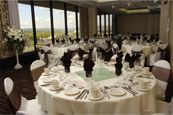 A banquet hall with round tables set for a formal event, featuring white tablecloths, silverware, and floral centerpieces.