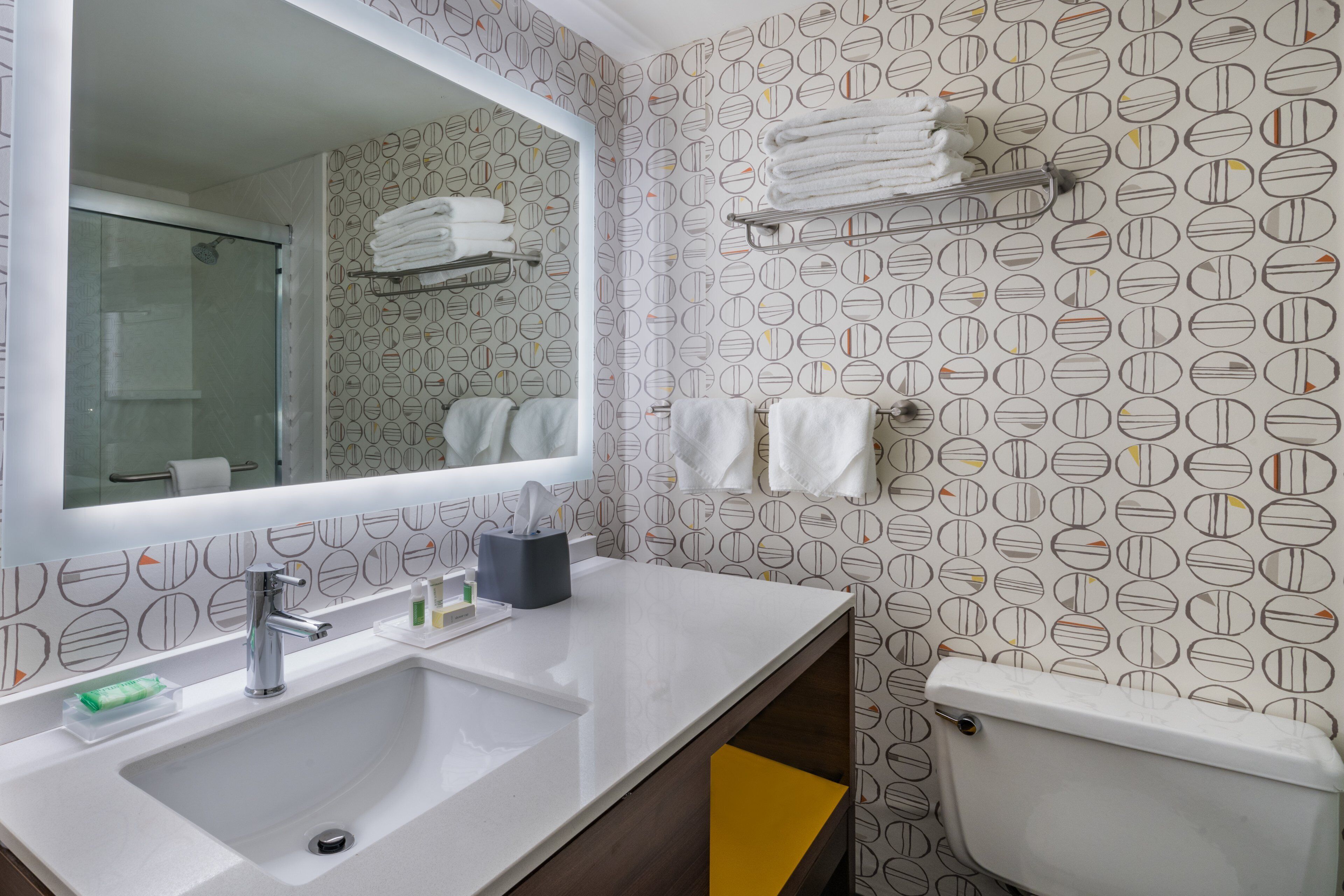 A modern bathroom with a large mirror, a sink, a toilet, and a towel rack.
