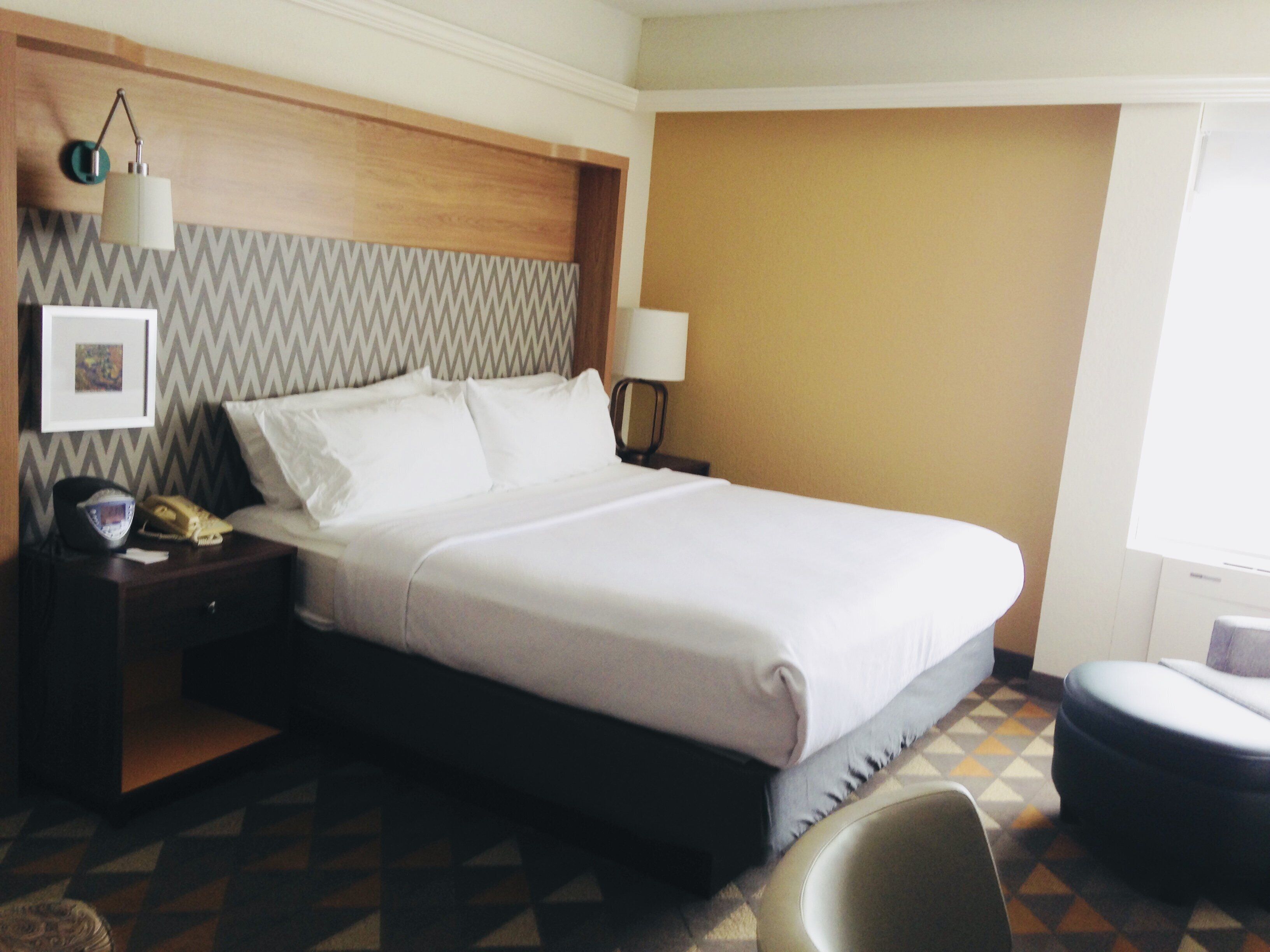 A hotel room with a bed, a nightstand, a lamp, a chair, and a window.