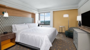 A hotel room with a large bed, a desk with a lamp, a television, and a view of the city. - Holiday Inn & Suites Pittsfield-Berkshires by IHG (Pittsfield)
