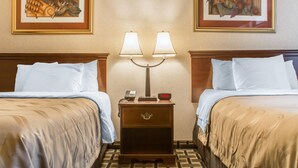 A hotel room with two beds, a nightstand with a clock and phone, and two wall-mounted lamps. - Quality Inn & Suites Palm Island Indoor Waterpark (Batavia)