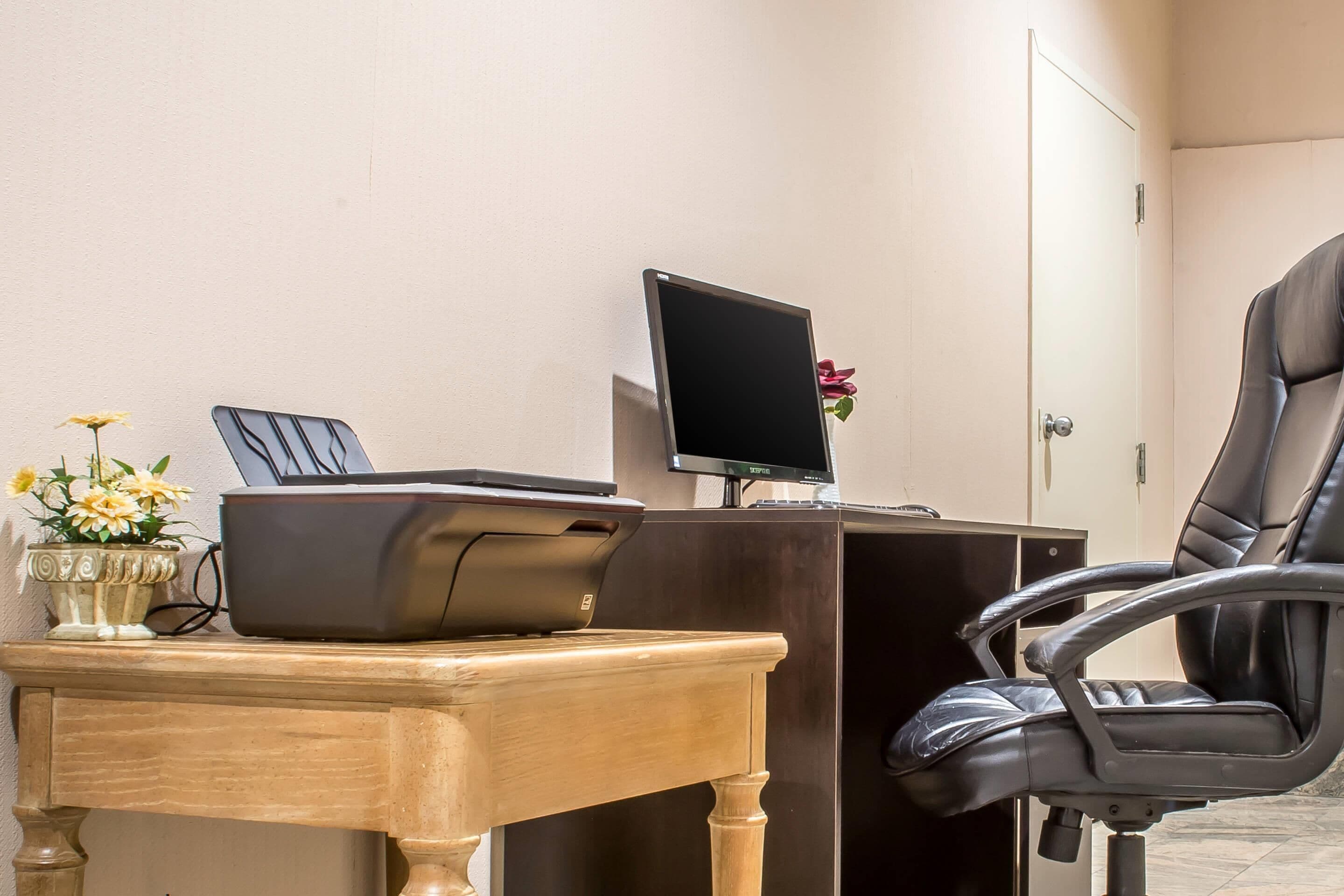 A desk with a printer, a computer monitor, and a chair.