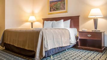 A hotel room with a bed, two bedside lamps, a nightstand, and a framed picture on the wall.