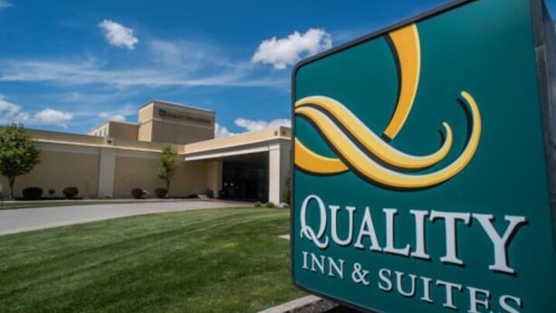 A sign for Quality Inn & Suites with a clear view of the building in the background. - Quality Inn & Suites Palm Island Indoor Waterpark (Batavia)