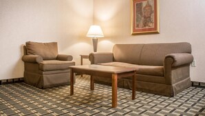 A room with a patterned carpet, two brown sofas, a small wooden table, a lamp, and a framed picture on the wall. - Quality Inn & Suites Palm Island Indoor Waterpark (Batavia)