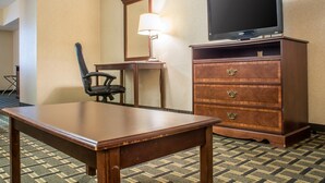 A hotel room with a wooden desk, a chair, a television on a wooden stand, and a dresser with drawers. - Quality Inn & Suites Palm Island Indoor Waterpark (Batavia)