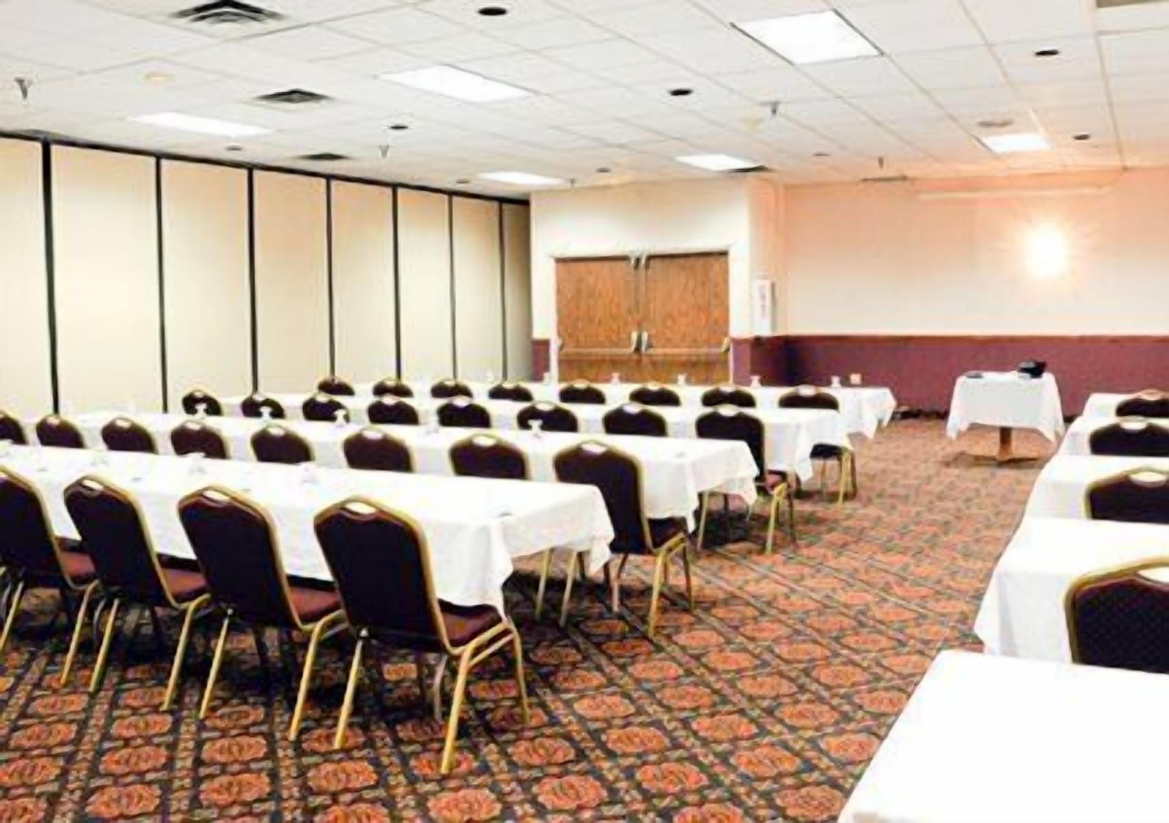 A conference room with rows of tables and chairs, carpeted floor, and a plain wall with a door.