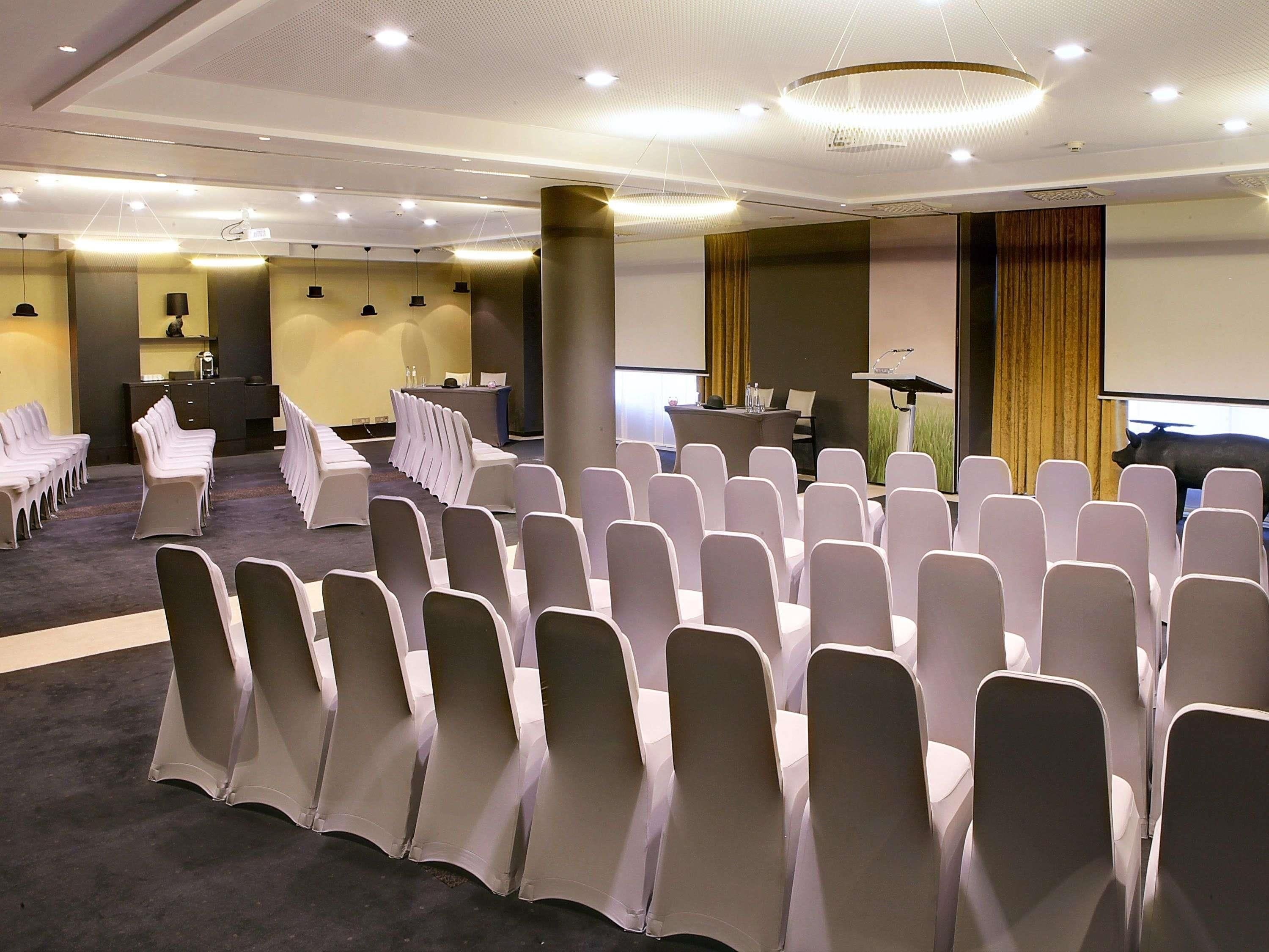Un salón de conferencias con filas de sillas, un atril y una pantalla para presentaciones.