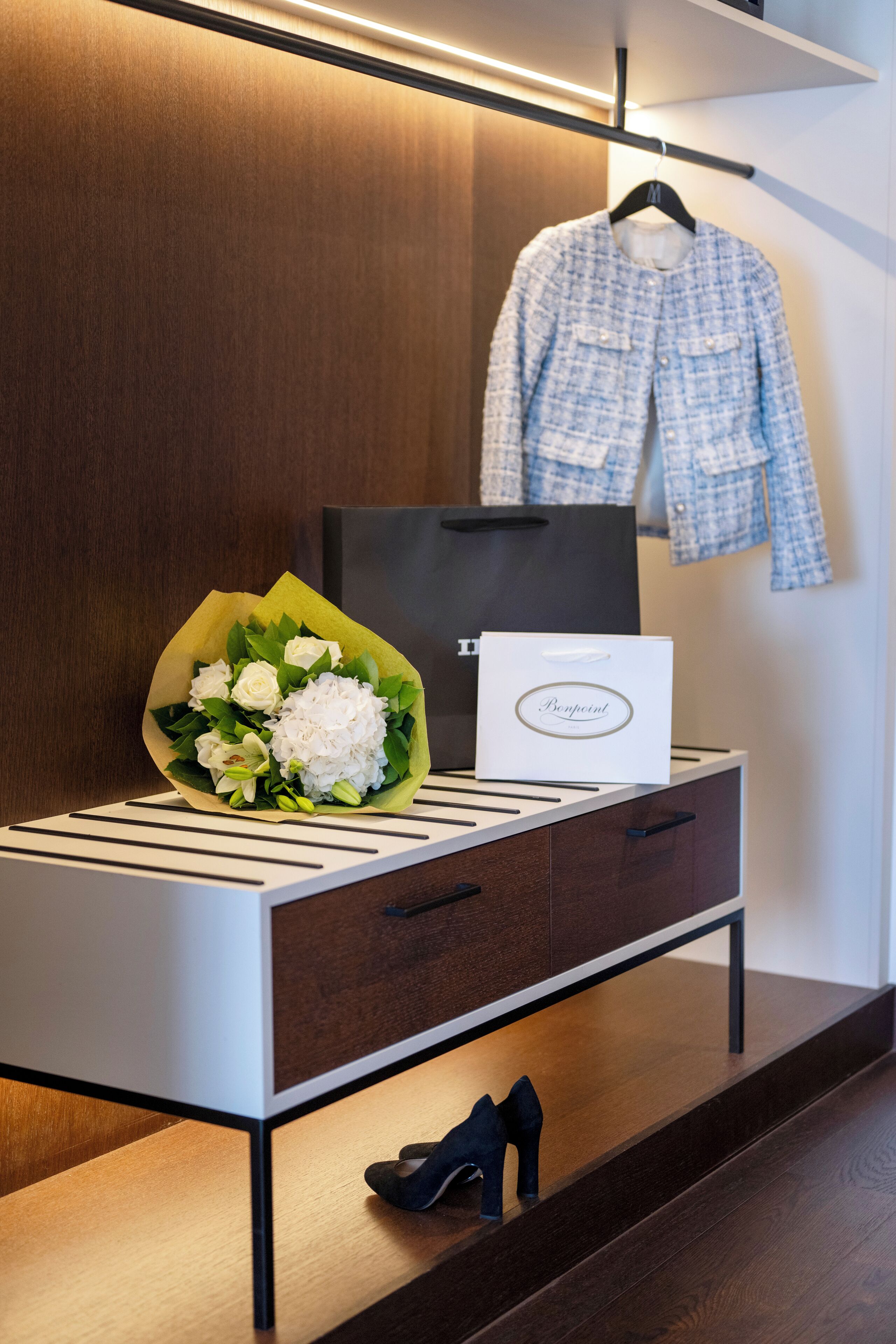 A wooden vanity with a mirror, a white handbag, a bouquet of flowers, and a pair of black shoes.