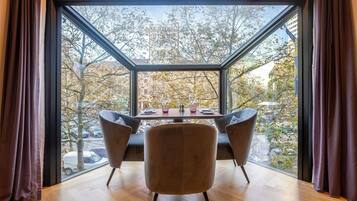 A dining area with a table and chairs, large windows, and a view of trees and buildings.