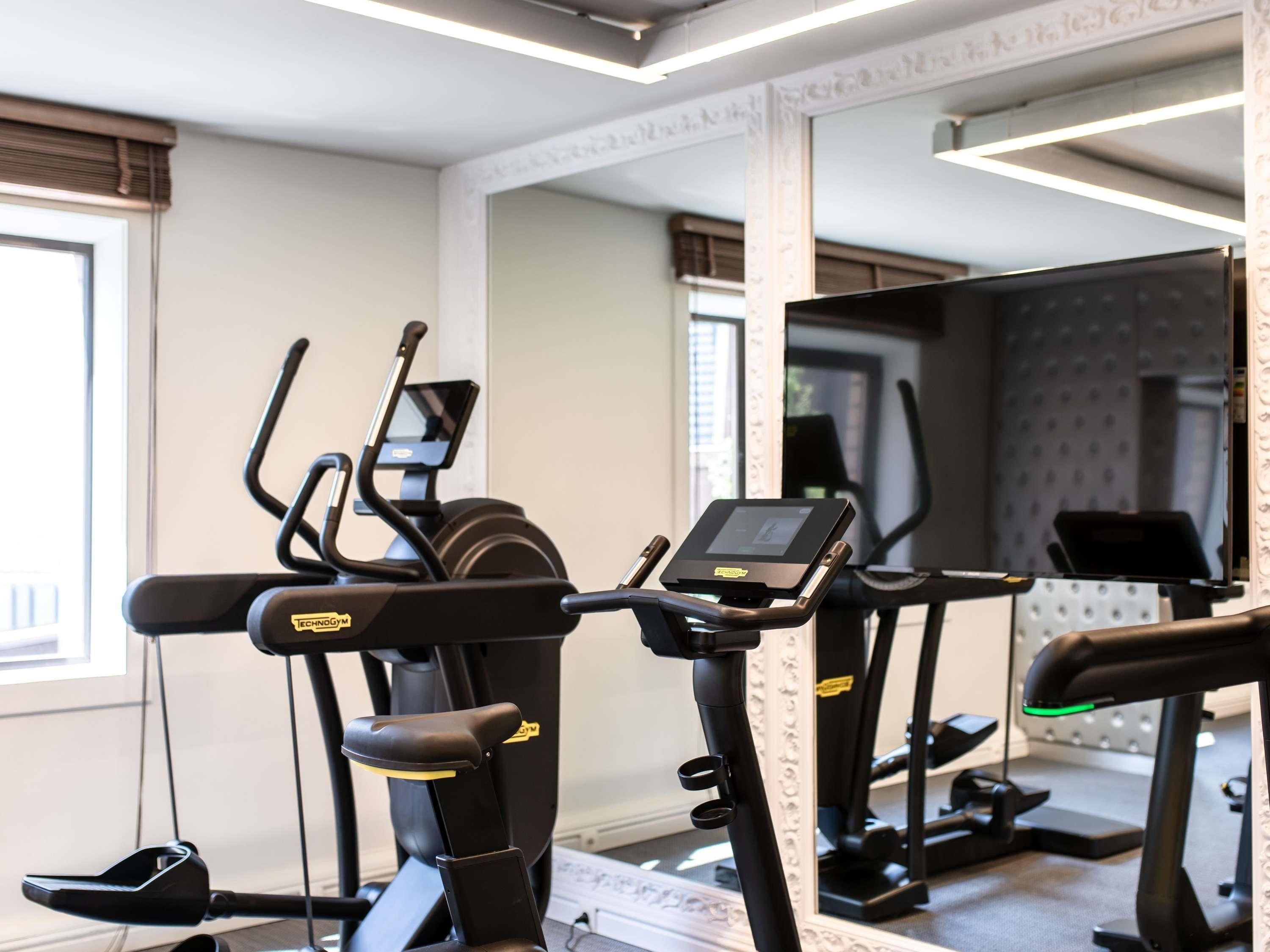 Een fitnessruimte met loopbanden en elliptische trainers, een spiegel en een raam met jaloezieën.