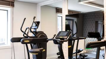 Een fitnessruimte met loopbanden en elliptische trainers, een spiegel en een raam met jaloezieën.