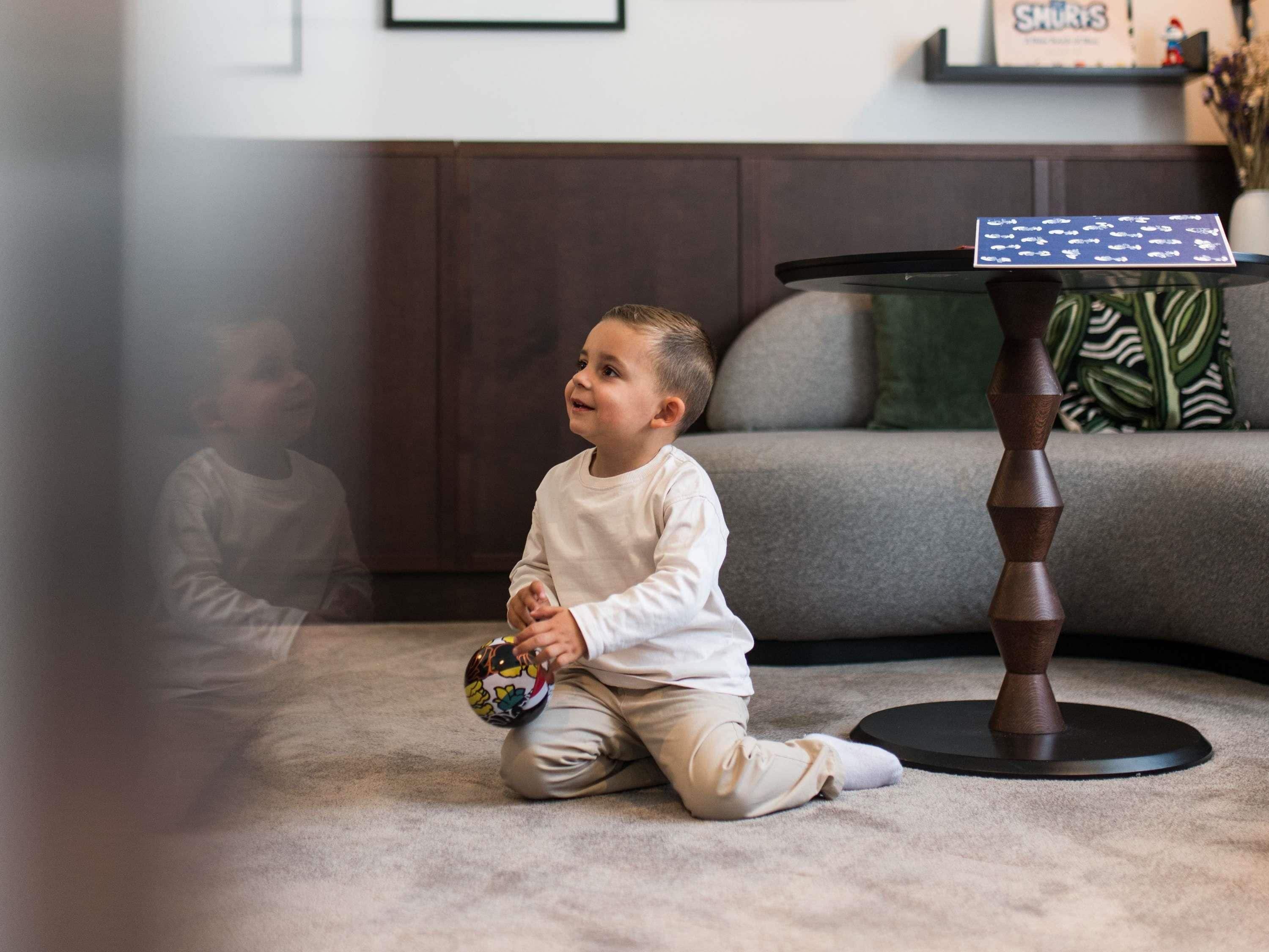 Un niño sentado en el suelo jugando con una pelota en una habitación con un sofá y una pequeña mesa.