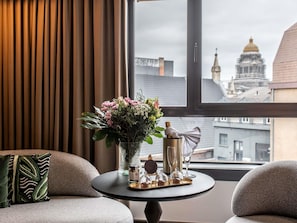 A room with a round table, a vase with flowers, a bottle, and a glass. - Le Louise Hotel Brussels - MGallery (Brussels)