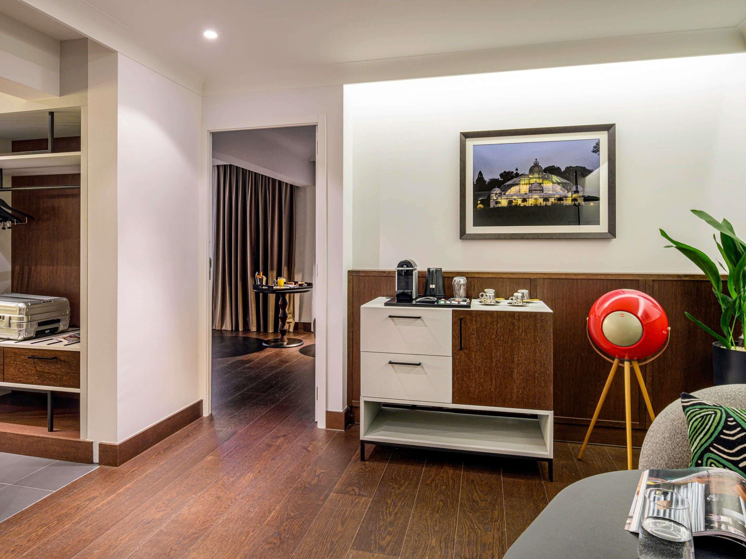 Una habitación de hotel moderna con suelo de madera, un escritorio con impresora, una lámpara roja y un cuadro en la pared.