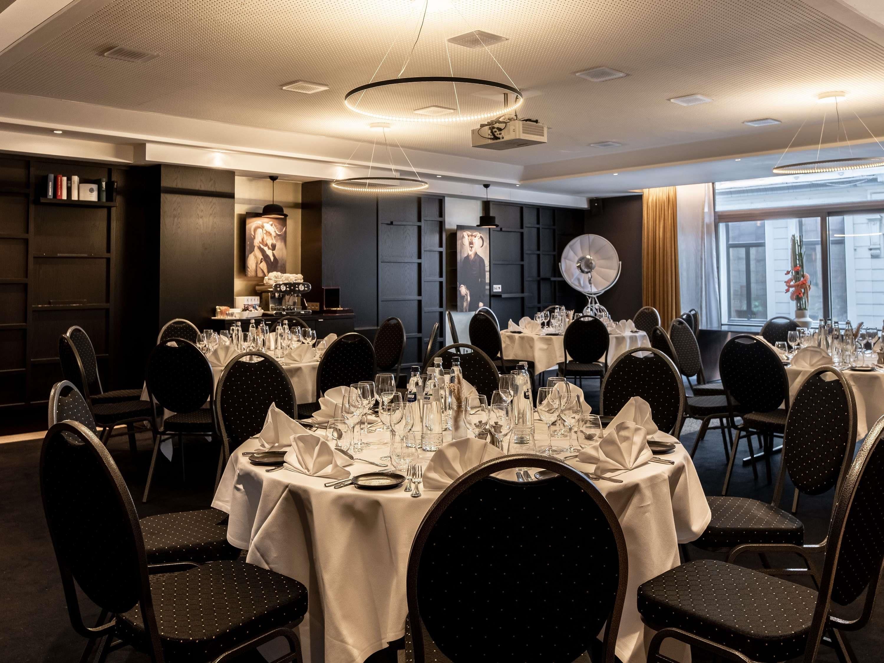A hotel dining area with round tables, black chairs, and a modern ceiling design.