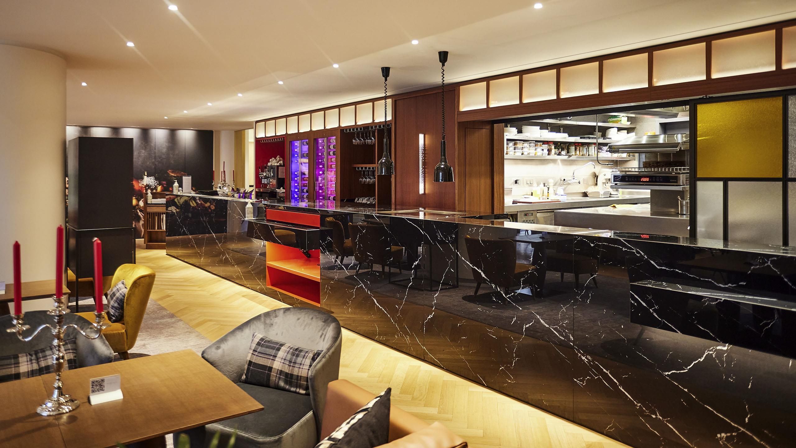 A modern bar area with seating and a kitchen in the background.