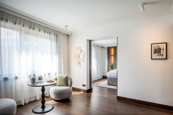 A hotel room with a round table, a sofa, a bed, and a large mirror. - Le Louise Hotel Brussels - MGallery (Brussels)