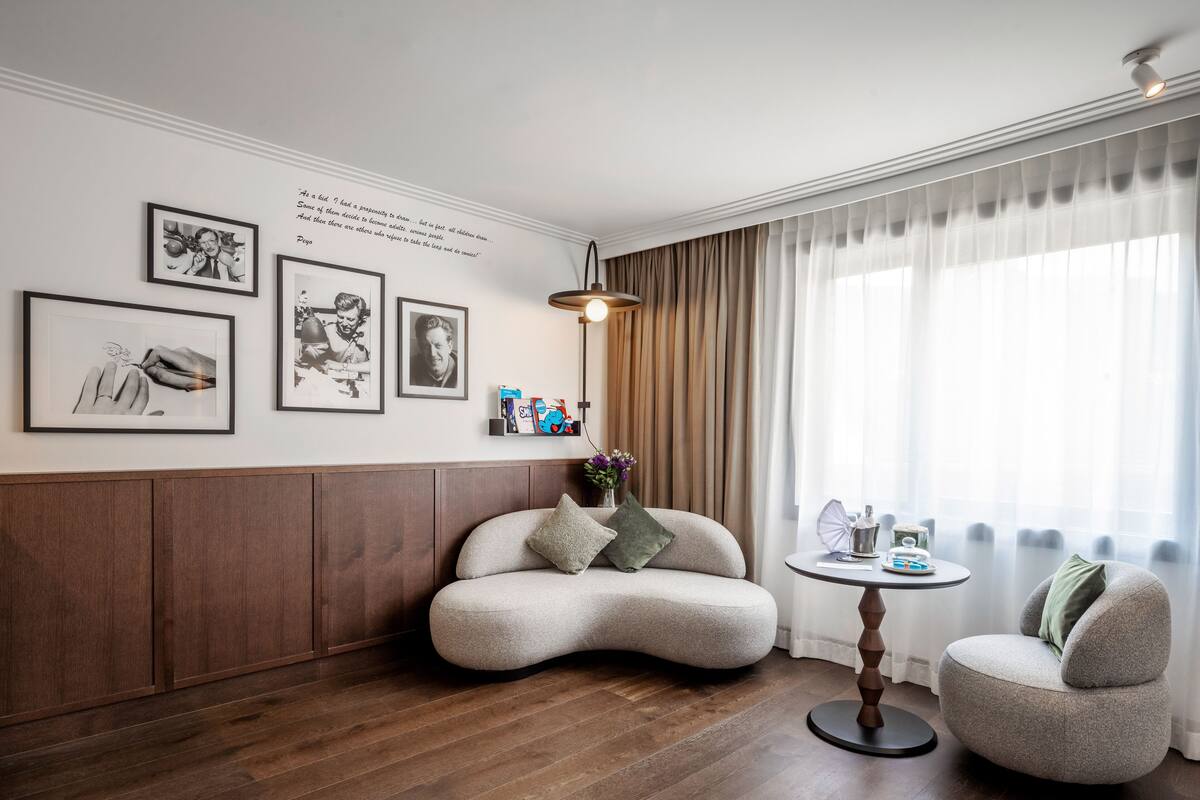 A modern living room with a curved sofa, a round table, and a small armchair. There are framed pictures on the wall and a lamp on the table.