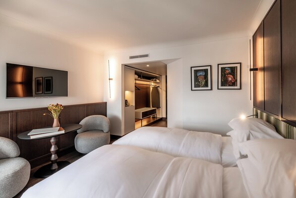 A modern hotel room with a large bed, a seating area with a table and chairs, a wardrobe, and a walk-in closet. - Le Louise Hotel Brussels - MGallery (Brussels)