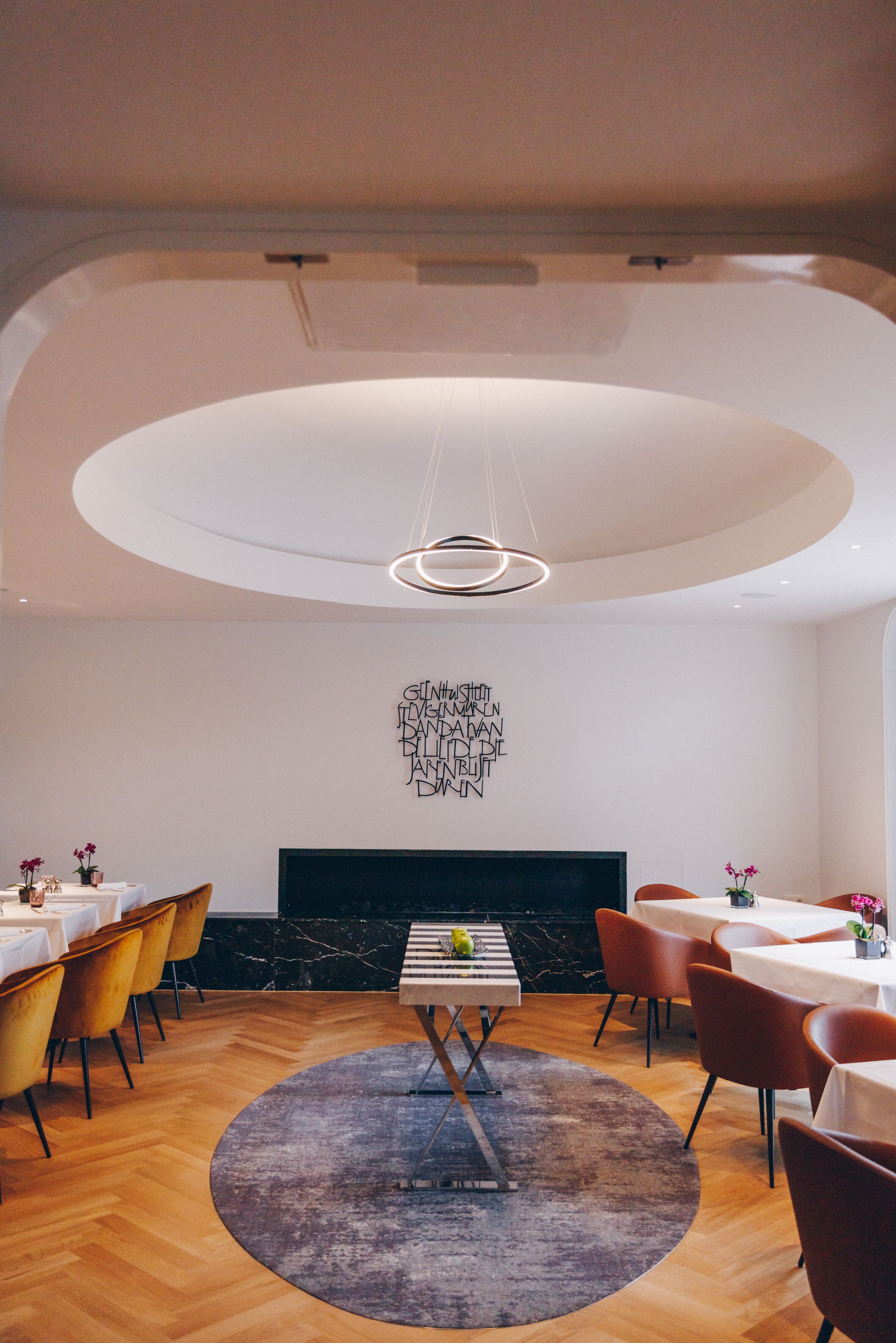 A modern dining area with a circular ceiling design, a fireplace, and a central table with chairs.