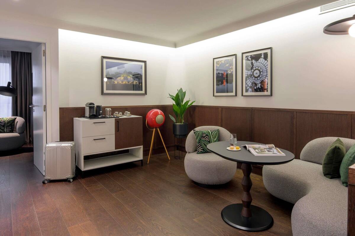 A modern hotel room with a kitchenette, a dining area with a round table, and two framed artworks on the wall.