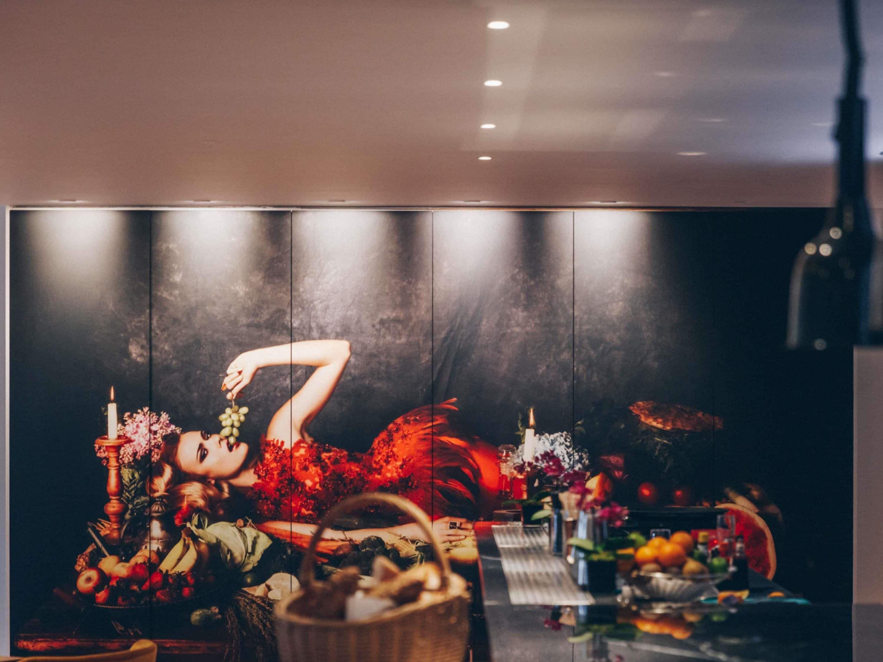 Una habitación con un separador de tonos oscuros, una mesa con frutas y una botella, y una obra de arte colgada en la pared.