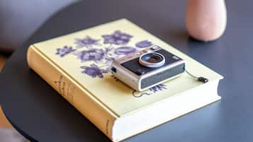 A book with a camera on top, a vase with flowers, and a couch in the background.