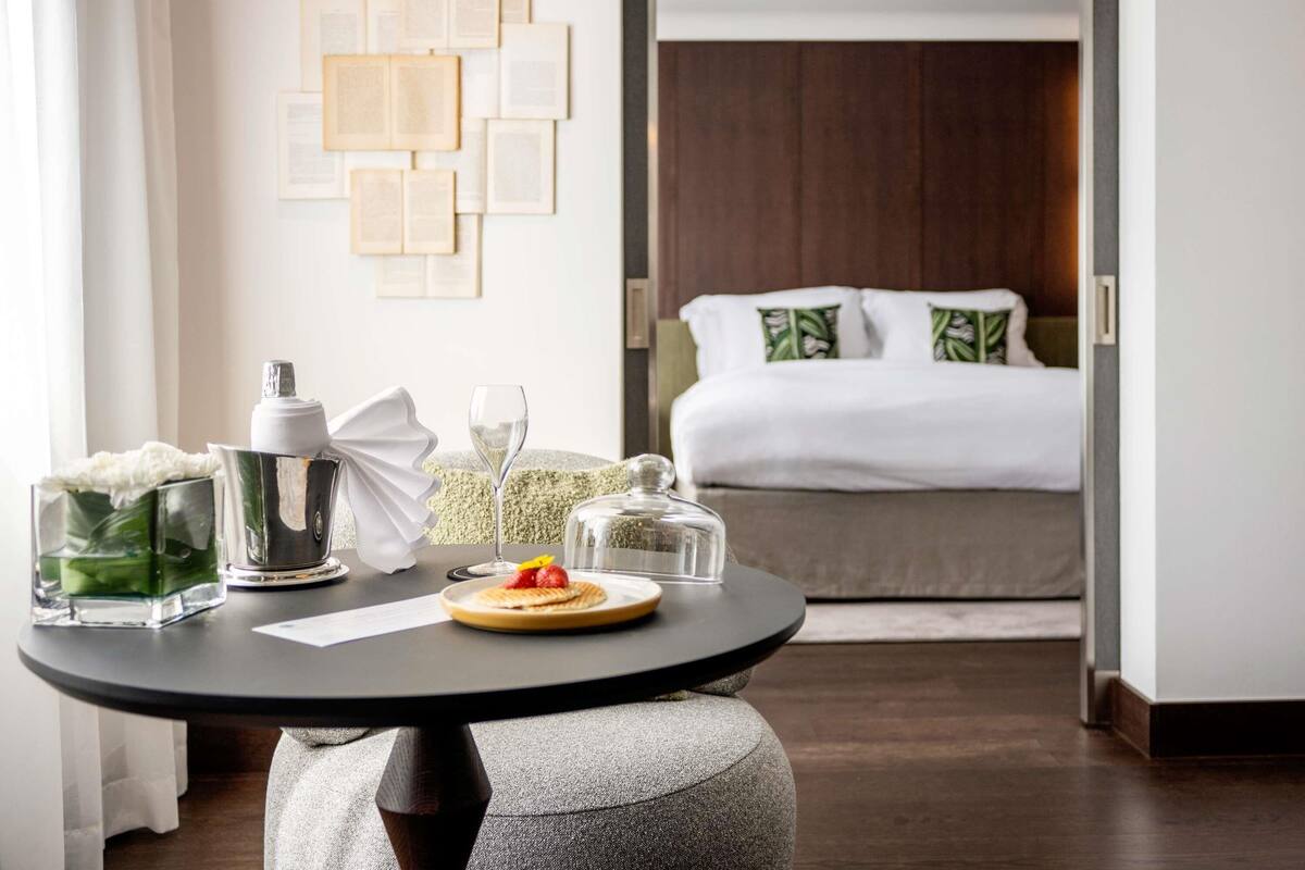 A hotel room with a bed, a bedside table with a glass, a bottle, and a plate with food.