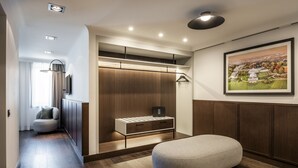 Una habitación de hotel moderna con suelo de madera, zona de estar, armario con iluminación integrada y un cuadro con paisaje en la pared.