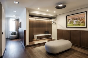 A modern hotel room with a wooden floor, a seating area, a wardrobe with built-in lighting, and a framed landscape painting on the wall. - Le Louise Hotel Brussels - MGallery (Brussels)