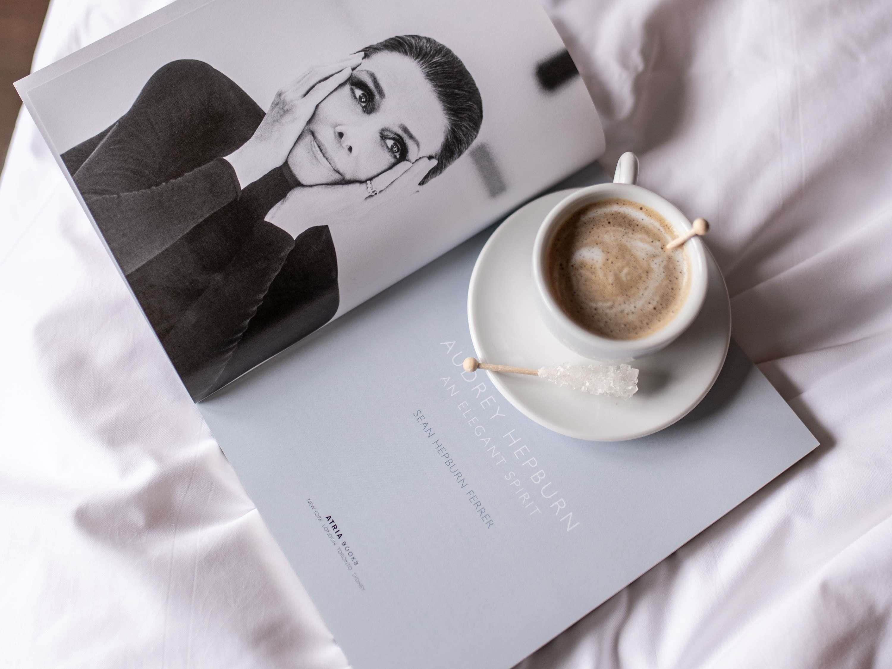 A book, a cup of coffee, and a spoon on a white surface.