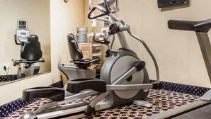 A gym with exercise equipment, a mirrored wall, a clock, and a television. - Econo Lodge Darien Lakes (Corfu)