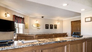 A hotel reception area with a marble counter, wooden cabinets, a flat-screen TV, and framed awards on the wall. - Econo Lodge Darien Lakes (Corfu)
