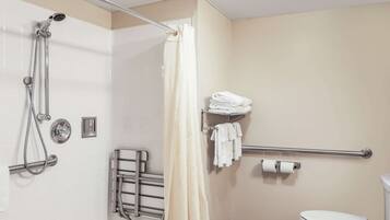 A bathroom with a shower, toilet, towel rack, and handrail.