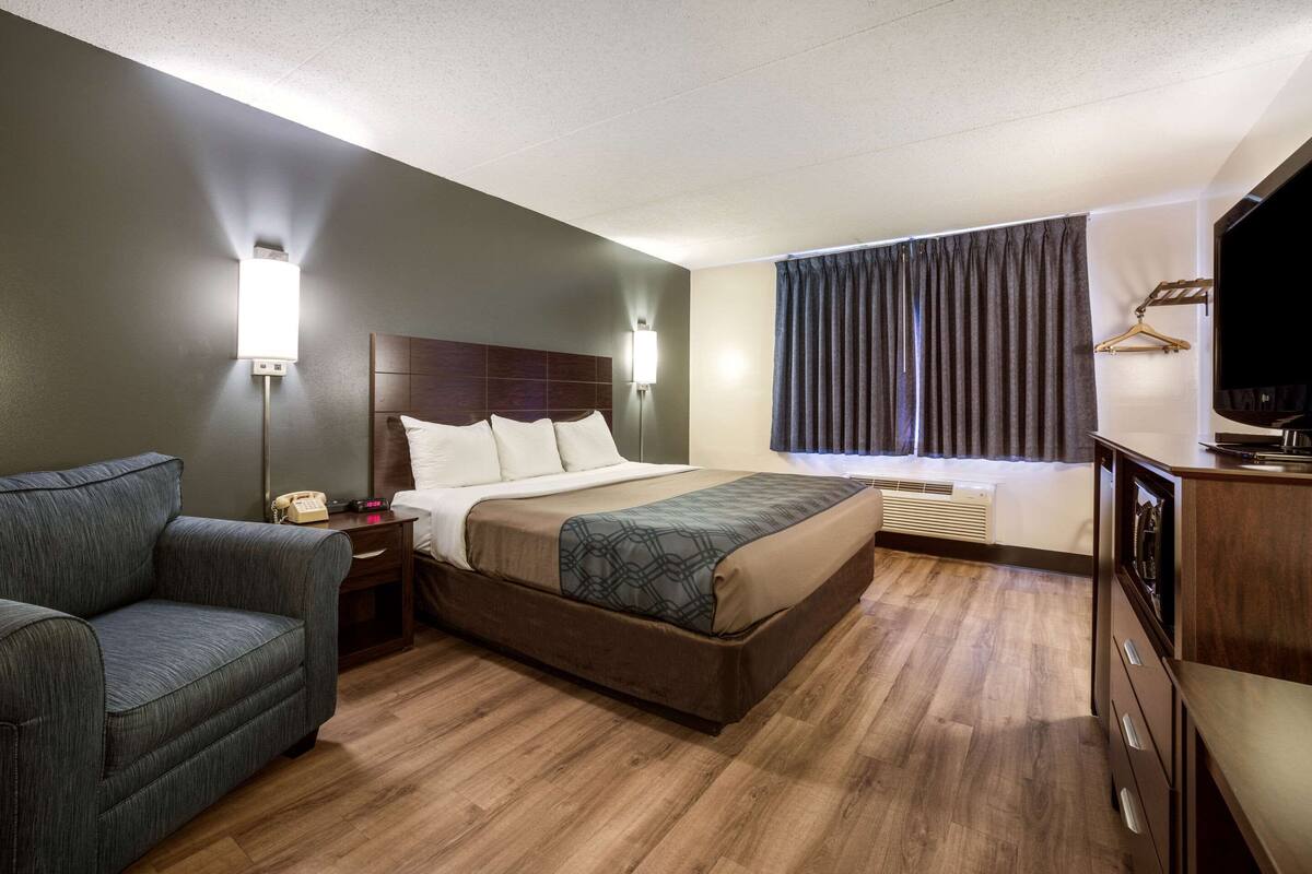 A hotel room with a bed, a sofa, a desk with a TV, and a window with curtains.