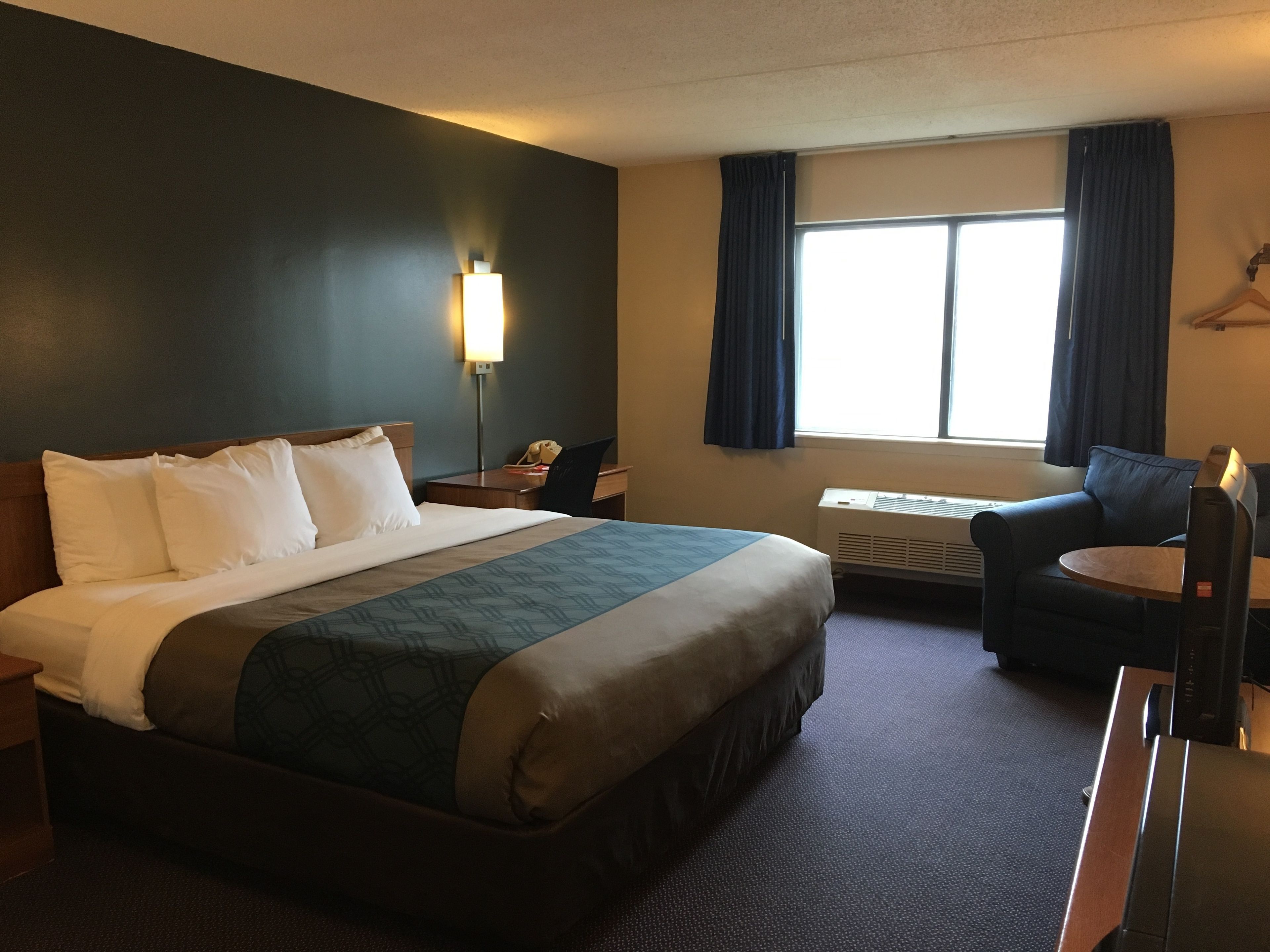 A hotel room with a bed, a desk, a chair, a lamp, and a window with curtains.