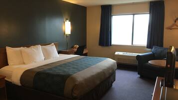 A hotel room with a bed, a desk, a chair, a lamp, and a window with curtains.
