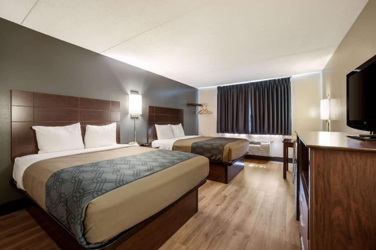 A hotel room with two beds, a desk, a television, and a window with curtains.