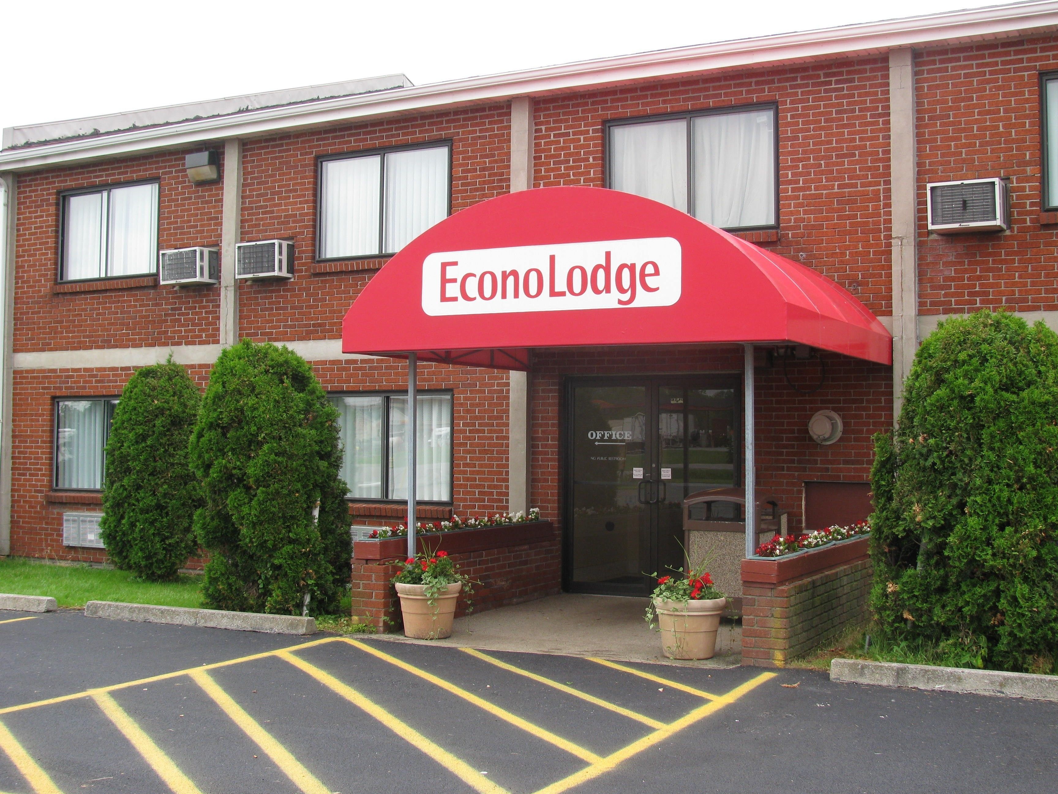 A brick building with a red awning labeled "Econo Lodge." There are two potted plants with red flowers in front of the entrance.