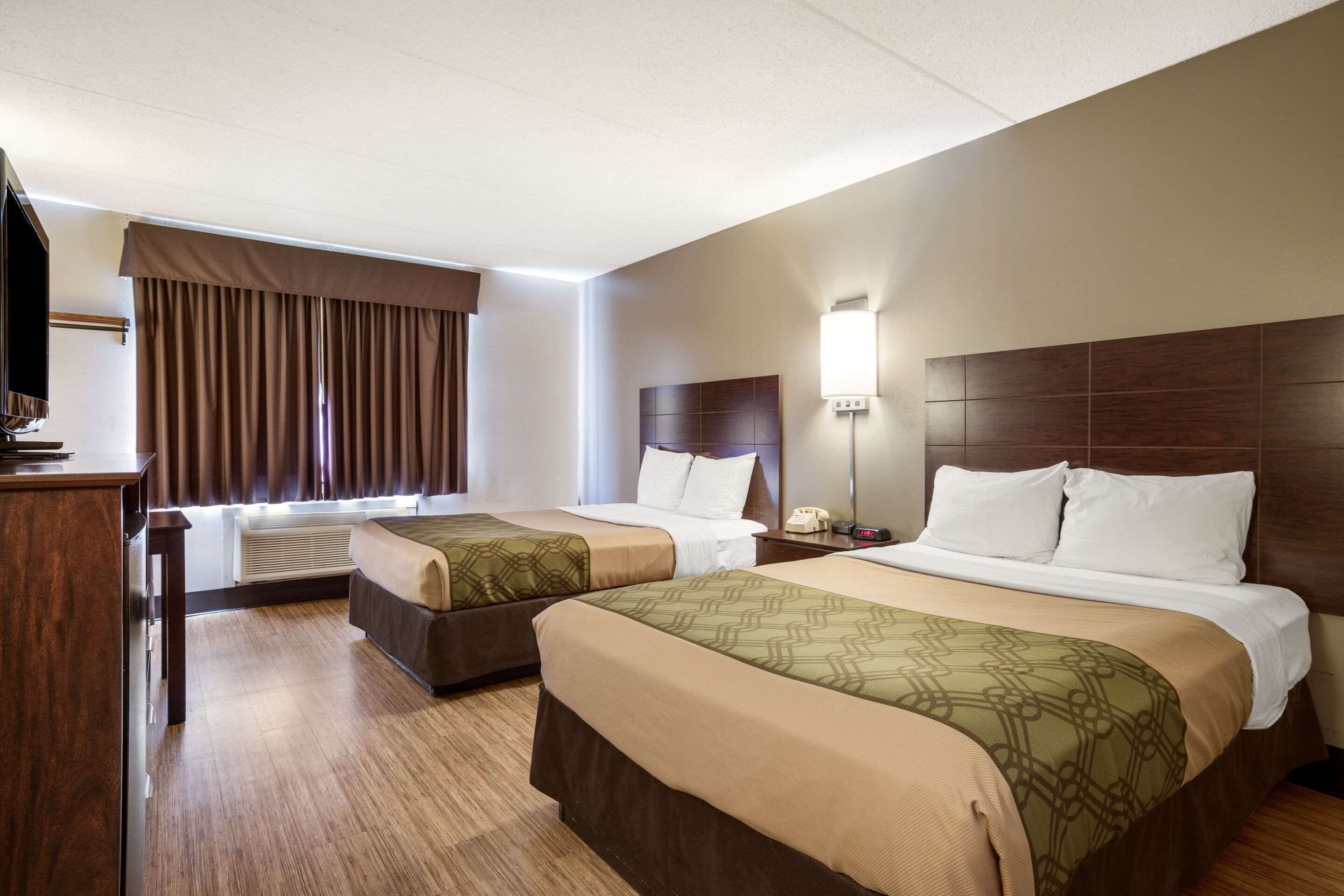 Habitación de hotel con dos camas, un escritorio, un televisor de pantalla plana, una lámpara y una ventana con cortinas.