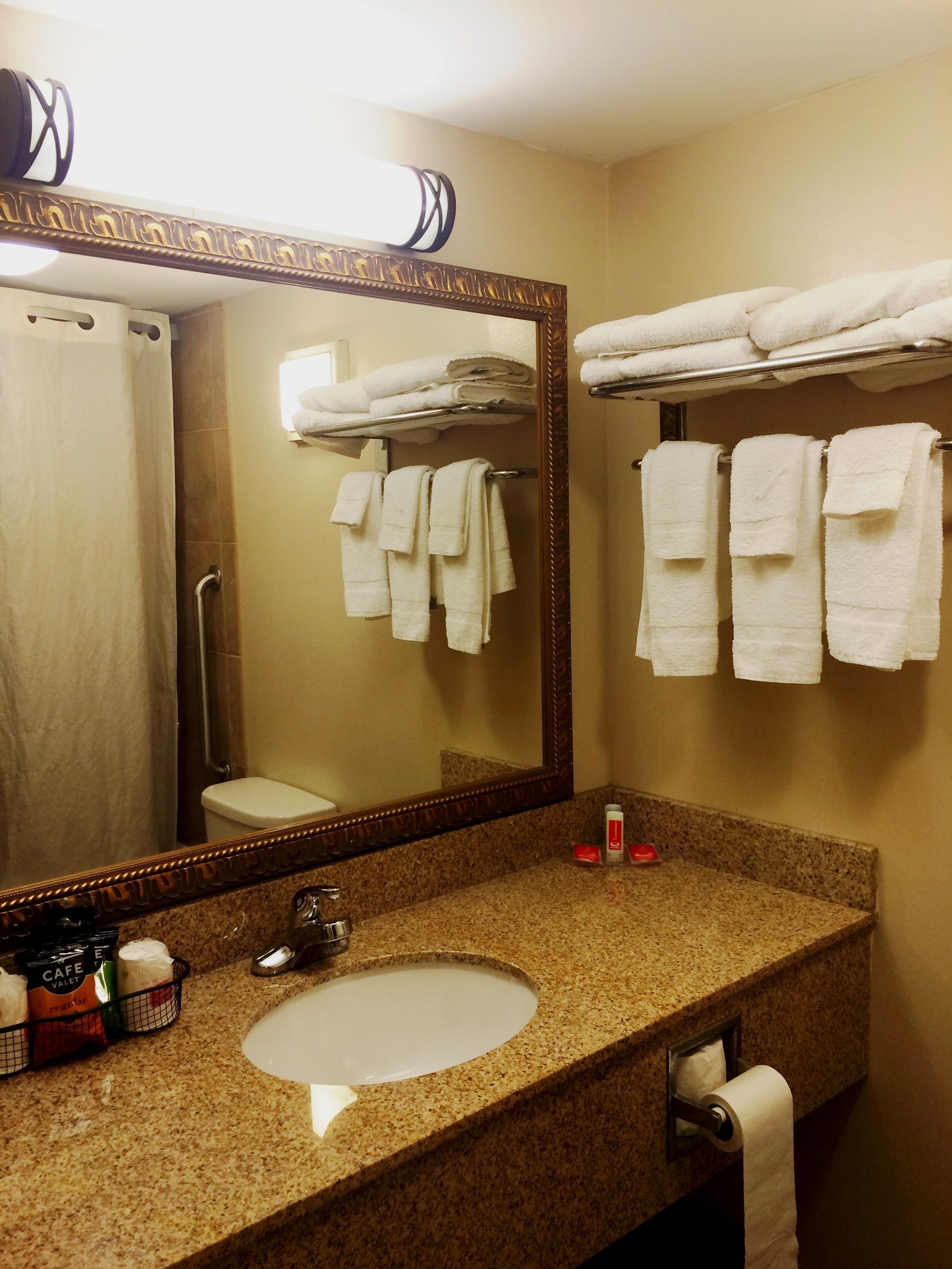 A bathroom with a granite countertop, a sink, a mirror, and multiple white towels hanging on racks.