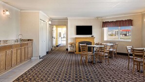 A hotel room with a kitchen area, a fireplace, a dining table with chairs, and a television mounted on the wall. - Econo Lodge Darien Lakes (Corfu)