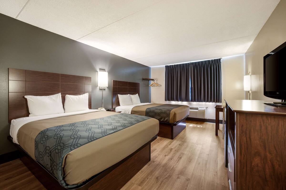A hotel room with two beds, a desk, a TV, and a window with curtains.